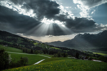 Sunbeams through clouds above mountain meadows