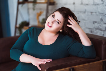 Happy plus size fashion model in green dress in the interior, fat woman at home