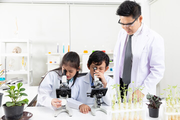 science teacher helping or teaching how to use microscope with child students in laboratory classroom