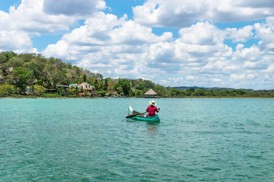 Fisherman in canoe boat in lake Itza rowing towards village with sunny cloud sky, El Remate, Peten, Guatemala