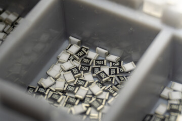 Grey scattered microscopic SMT surface mount chip resistors sorted in grey storage container