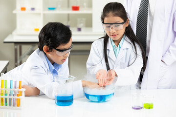 child students doing or testing a chemical experiment with science teacher by them side in laboratory classroom