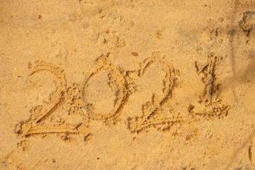 Photo of wave washing out 2021 numbers written on wet sand at beach. Concept of New Year, Christmas and travel on winter holidays.