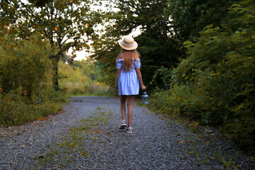Fototapeta na wymiar Little cute girl in a straw hat. Evening forest walk with an ancient lantern in his hands. Summer, sunlight, portrait, warm, forest.