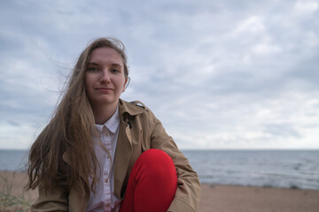 pretty girl sitting on a beach in beige trench coat