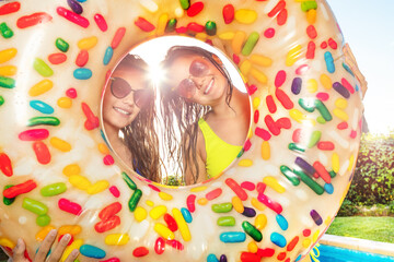 Two girls 16 years old smile looking out from inside inflatable doughnut wearing sunglasses