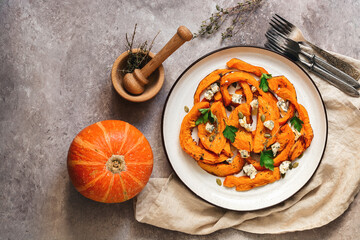 Baked pumpkin with herbs and blue cheese in a plate on a beige rustic background. Top view, flat lay, copy space.