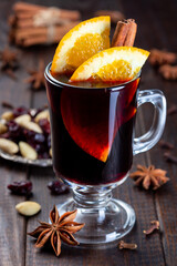 Red glogg or mulled wine with orange slices and cinnamon stick on dark wooden background, vertical, closeup