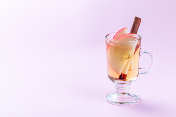 Glass of white glogg or mulled wine with apple slices and cinnamon stick on a pink background, horizontal, copy space