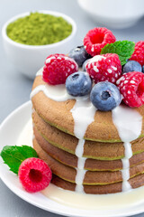Matcha pancakes served with condensed milk, blueberry and raspberry on white plate, vertical, closeup