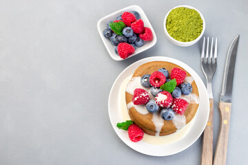 Matcha pancakes served with condensed milk, blueberry and raspberry on white plate, horizontal, top view, copy space