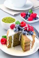 Cuted stack of matcha pancakes served with condensed milk, blueberry and raspberry on white plate, vertical