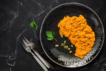 Pumpkin puree with herbs and seeds on a plate, black stone background. Top view, flat lay, copy space.
