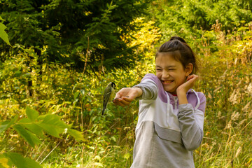 Laughing girl feeding birds in autumn forest. The concept of spending a joint family weekend in nature.