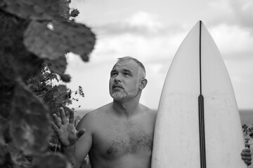 Black and white portrait of handsome shirtless man surfer, holding white surf board  and cactus on background