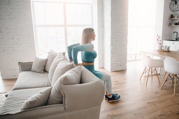 Slim sporty athletic girl does push-up exercises with improvised sofa objects at home. Concept Lifestyle sports for pandemic