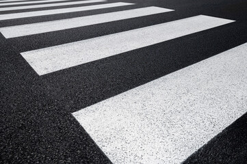 Particular pedestrian crossing, asphalt road, white stripes on a dark gray background, zebra stripes, perspective views, black and white.