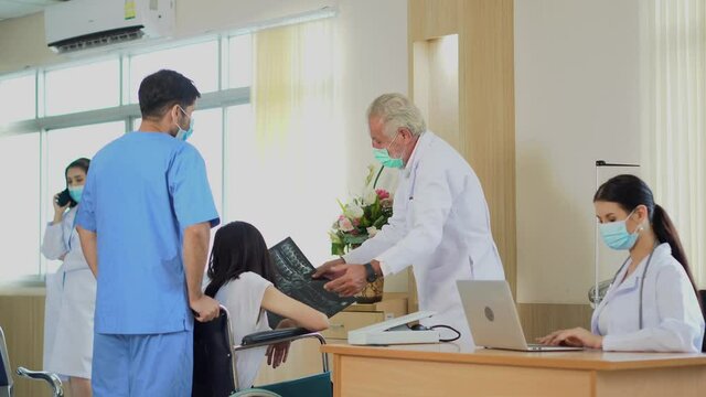 group of diverse medical team wearing surgical face mask explaining X-ray results with patient on wheelchair in hospital . new normal during  Coronavirus pandemic or Covid-19 outbreak