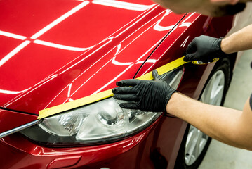 Car service worker applying protective tape on the car details before polishing.