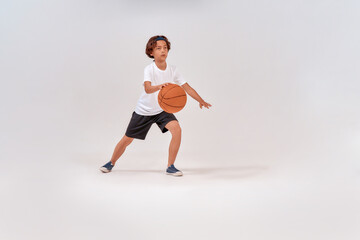 Fototapeta na wymiar Favourite sport. Full-length shot of a teenage boy playing basketball while standing isolated over grey background, studio shot