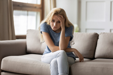 At least minute of rest. Exhausted young female sits on sofa alone suffering from headache or...