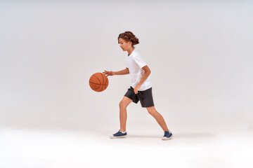Little winner. Full-length shot of a teenage boy playing basketball while standing isolated over...