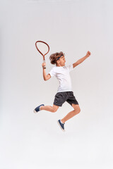 Full-length shot of a teenage boy jumping with a tennis racket isolated over grey background,...