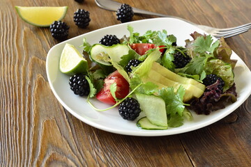 Avocado, blackberry, fresh herbs, сucumber and tomato salad with lime dressing, copy space