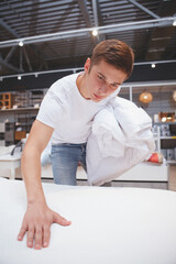 Vertical shot of a charming man shopping at furniture store, examining besheets on sale at department store