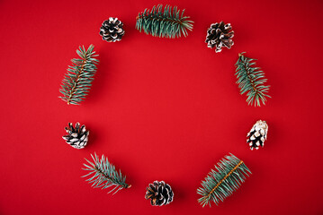 Christmas composition. Wreath made of fir tree branches and festive pine cones on a red background, top view