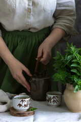 Mint tea in a vintage Chinese tea set, a woman in a linen dress and an apron, and a bouquet of mint in a jug.