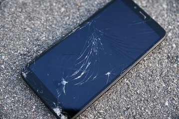 Damaged smartphone with broken touch screen on asphalt