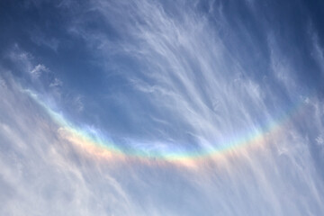Smiling rainbow in the blue sky on sunny day with light clouds