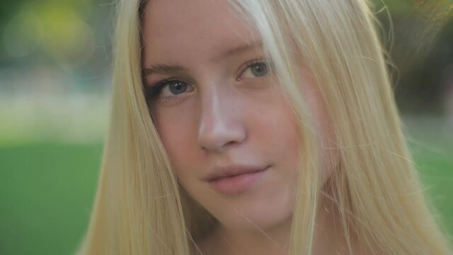 Close-up portrait of a beautiful Caucasian girl with blue eyes, no makeup, with blond hair, smiling sweetly and looking at the camera at sunset. The concept of aesthetics and health.