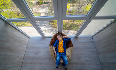 Little boy relaxing on a terrace. Teenage dreaming of summer vocation looking through the glass wall. Having nap in soft chair.