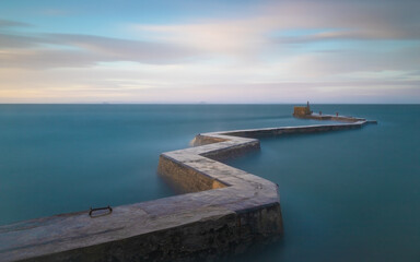 Obraz premium A long exposure shot of the zigzag breakwater at St Monans during some stormy weather - the long exposure smooths out the water giving the appearance of calm