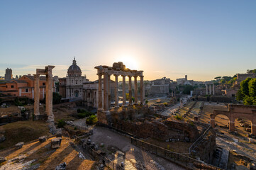 Obraz premium Silent dawn in the Roman Forum, Rome. The sun's rays appear from the temple of Saturn and illuminate the buildings, the Arch of Severus, the temple of Vesta, the Arch of Titus, the Coliseum. Italy.