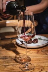 A hand is pouring wine into red wine glass 