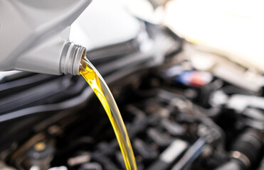 Pouring fresh automotive engine oil (lubricating oil, yellow liquid oil) into a motor car with a blurred engine background. Change new oil. Maintenance, service, and energy fuel concept. .