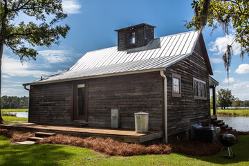 Obraz premium Rear scenic view of the exterior of a rural rustic wooden camp house used for fishing and hunting. The house is located on a large pond