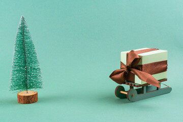 The gift lies on the sleigh next to the Christmas tree on turquoise background . christmas concept. postcard.