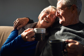 Loving Senior Couple Relaxing And Chatting On Sofa At Home Together With Hot Drink