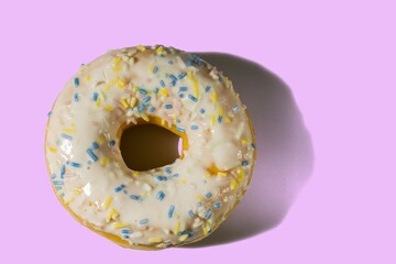 Close up view of donut sprinkled with multicolored glaze isolated on pink background. Food and drink concept.