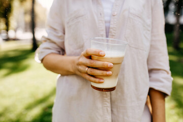 Person holding a plastic cup of ice coffee, outdoors.