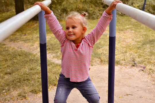 A cute little girl plays on the playground on an autumn day. Baby hanging on parallel bars