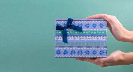 Female hands holding blue gift box decorated with blue ribbon on turquoise background.christmas concept. copy spase