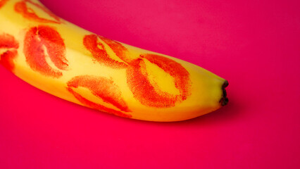 Red lipstick on a yellow banana on a pink background. Love and sex concept.