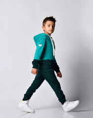 Boy in tracksuit, sneakers walking isolated on grey