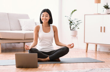 Millennial woman meditating with trainer online on laptop