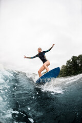 Active woman stands with bent knees on surfboard and ride on wave